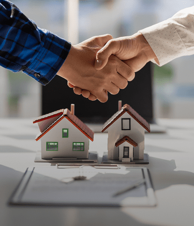 Two people shaking hands over a table with two small model houses and an open document.
