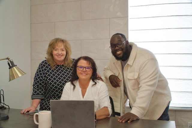Three people are sitting at a table with a laptop.